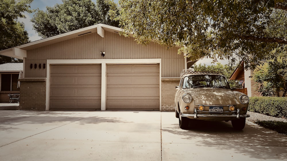 An image of a car parked outside a house with two garage doors